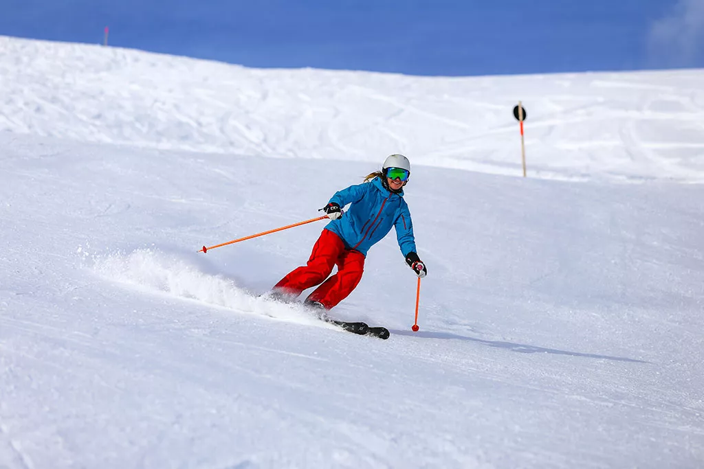 Mujer sonriente esquiando con todo el equipo de esquí en un día soleado