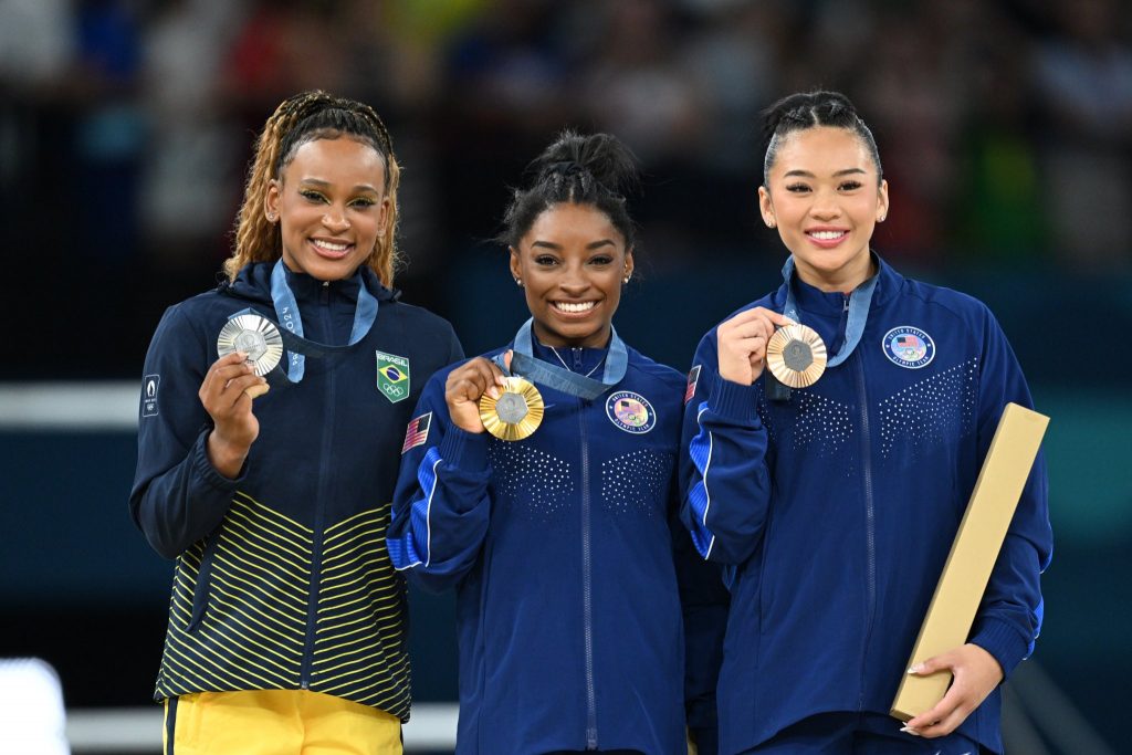 Simone Biles en el centro del podio junto a Rebeca Andrade y Sunisa Lee tras la final individual all-around en París 2024.